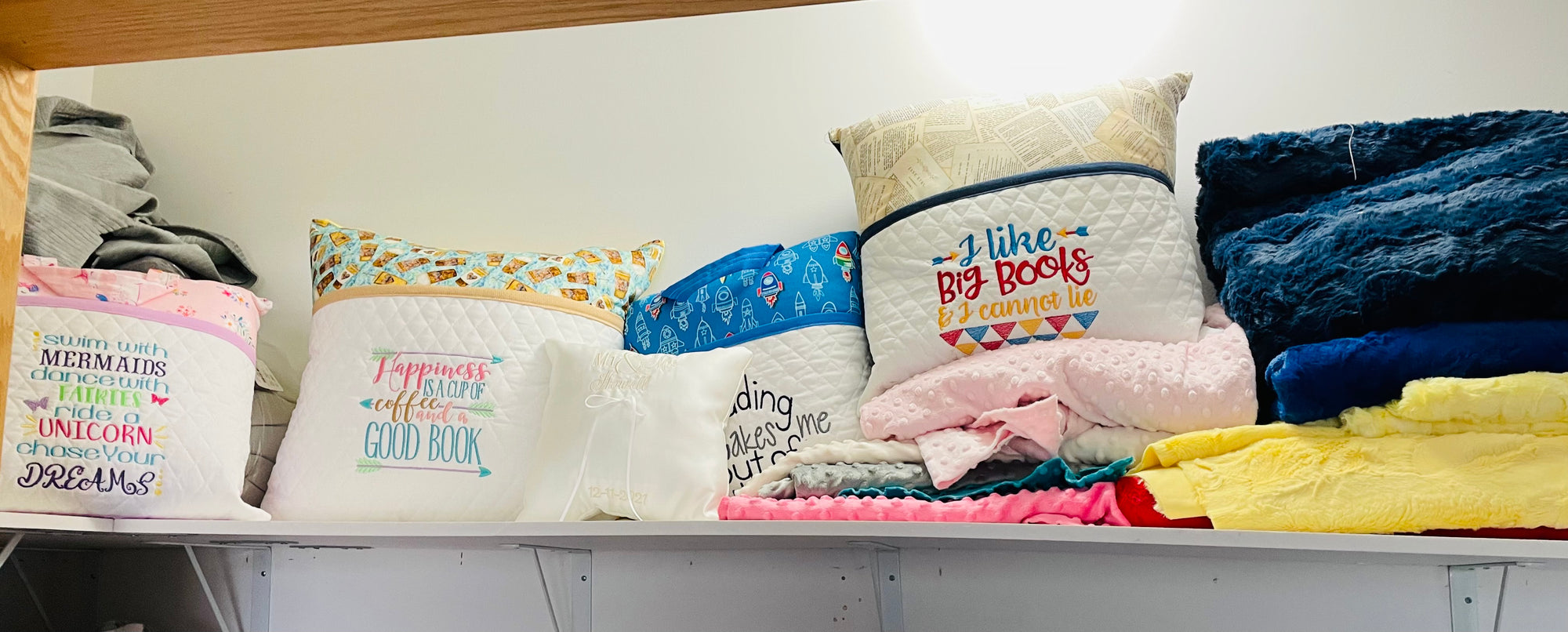 4 book pillows with a machine embroidered saying on a shelf