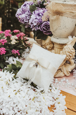 Satin ivory ring pillow with a lace overlay. Beautiful Ivory bow holding the rings. Sitting on a bed of flowers.