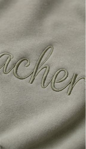 Close-up of a sage green fabric surface with cursive embroidered lettering partially visible.