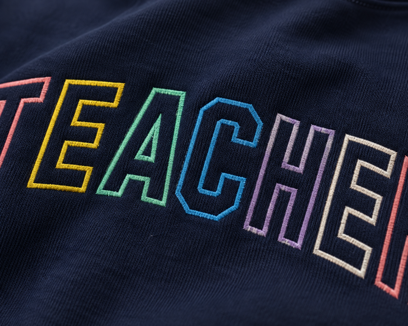 Close-up of a navy blue sweatshirt featuring the word 'TEACHER' embroidered across the chest in rainbow colors.